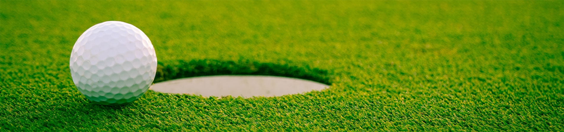 A golf ball near a hole on a green turf, highlighting the putting area in a golf course setting.